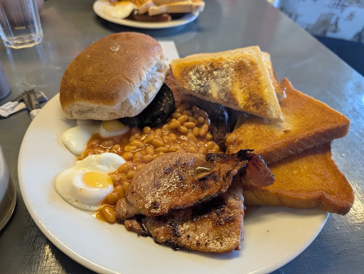 A breakfast plate: two fried eggs, beans, bacon, black pudding, buttered toast and a soft roll.